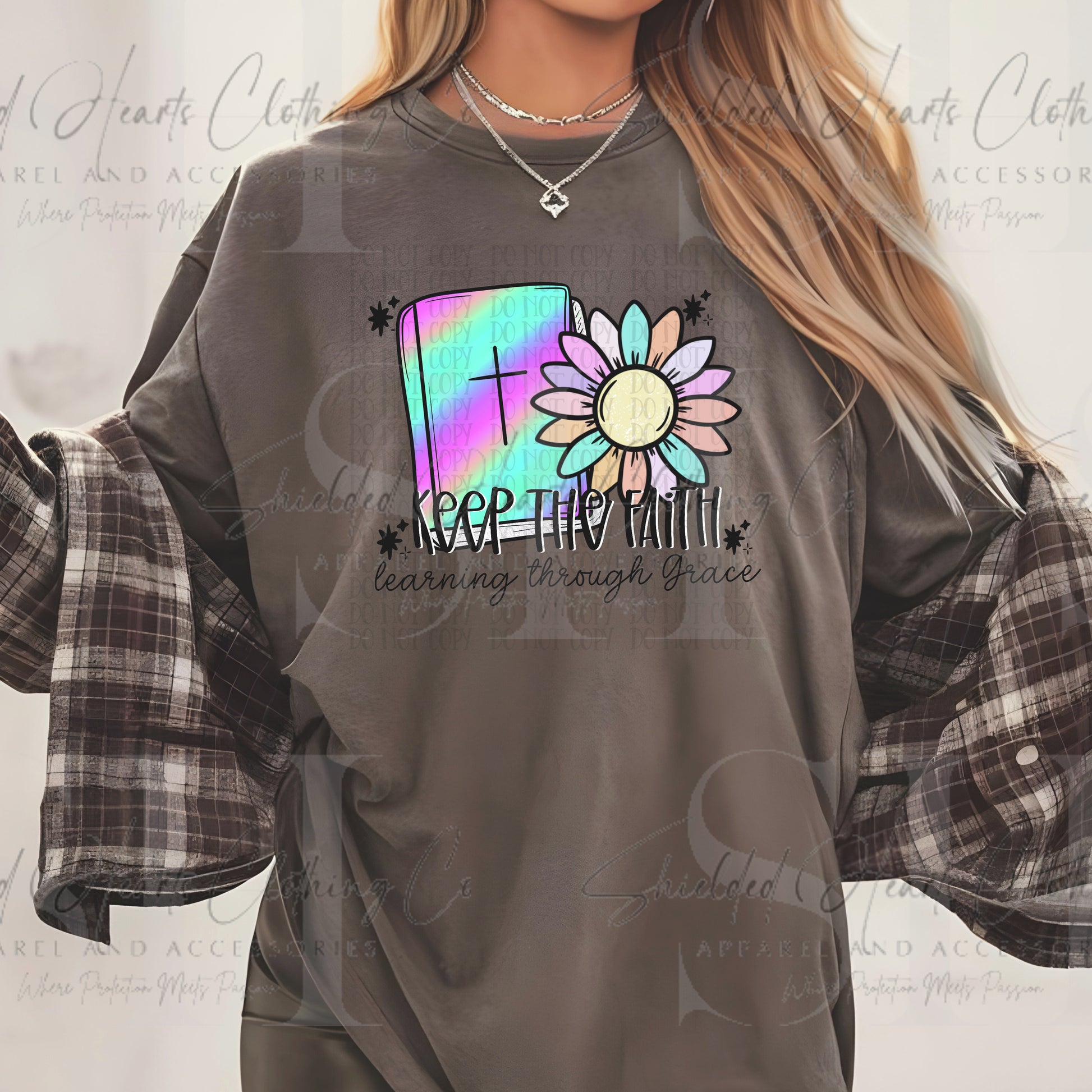 A woman wearing a dark gray graphic t-shirt featuring a colorful book and sunflower design with the text 'KEEP THIS WITH learn my through Grace', styled with a plaid flannel shirt underneath.
